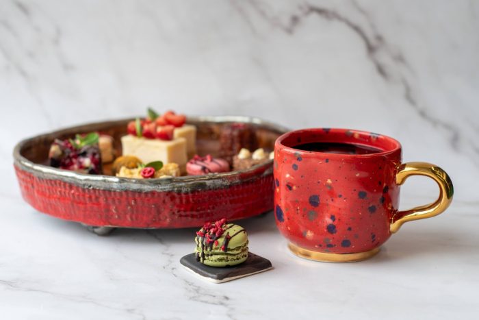 Dineris desertų rinkinys su mini desertais ir macaron šalia kavos puodelio, skirtas renginių kavos pertraukėlėms.