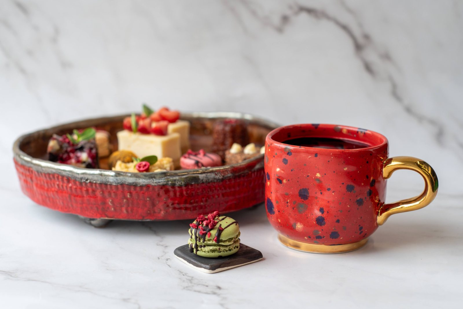 Dineris desertų rinkinys su mini desertais ir macaron šalia kavos puodelio, skirtas renginių kavos pertraukėlėms.